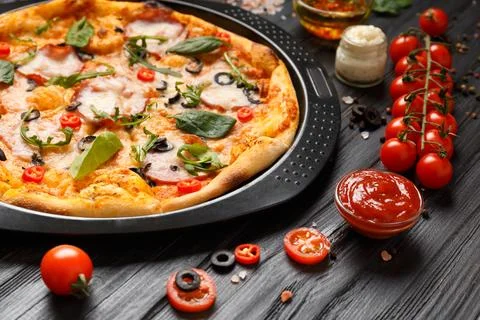 Pizza on a black baking dish on a dark wooden background. Stock Photos