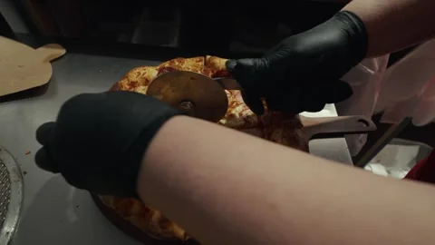 Pizza chef in black gloves slices freshly baked pizza with a pizza cutter on a Vídeo Stock 332736723