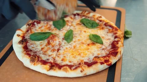 A pizza chef slices a cheese and basil pizza into four pieces using a speci.. Stock Footage 277890441