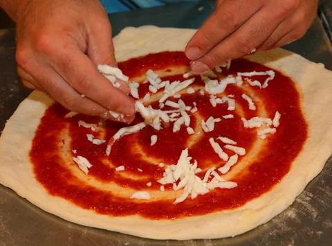 Pizza chef while he puts the mozzarella cheese on top of the pizza dough ty.. Stock-Fotos