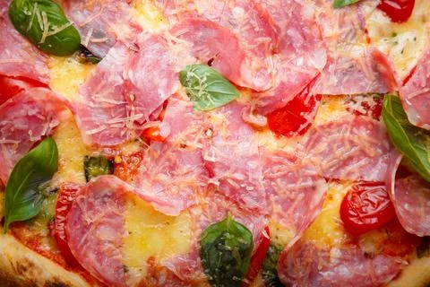 Pizza closeup texture, food pattern background. Ham, tomatoes, green basil Foto stock