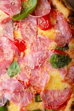 Pizza closeup texture, food pattern background. Ham, tomatoes, green basil Stock Photos