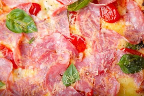Pizza closeup texture, food pattern background. Ham, tomatoes, green basil Foto stock