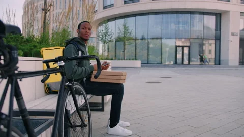 Pizza courier while waiting for a customer on a bench near the business center Stock Footage 217363873