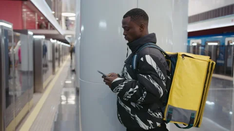 A pizza delivery man spends time on his phone while waiting for a subway car Stock Footage 239324443