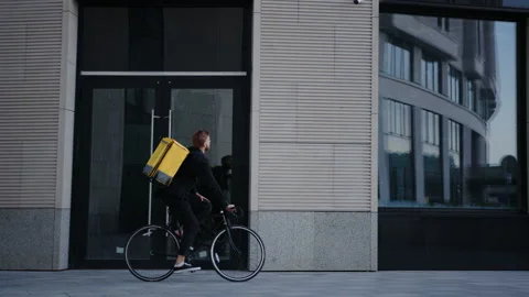 Pizza delivery man with a yellow backpack rides a bike around the city Stock Footage 219459172