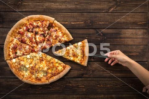 Pizza eating a hand taking one piece of pizza on a dark brown wooden backgrou Stock Photos