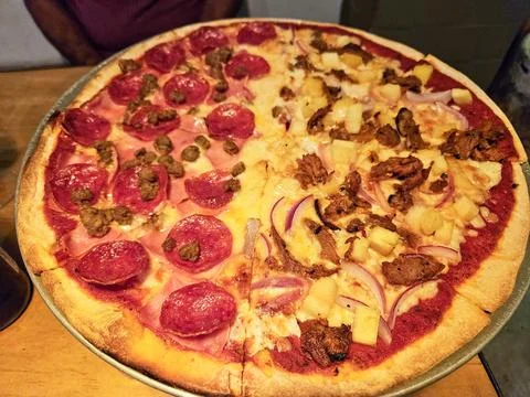 A pizza with four different toppings, including pepperoni, onions, pineapple Stock Photos