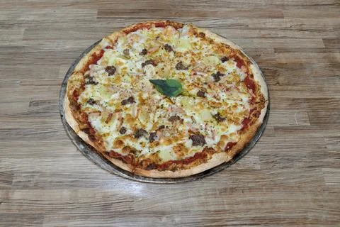 A pizza with a green leaf on top sits on a wooden table 스톡 사진