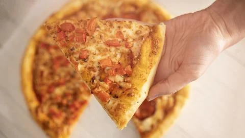 Pizza in hand on a light background. Close-up. Stock Photos