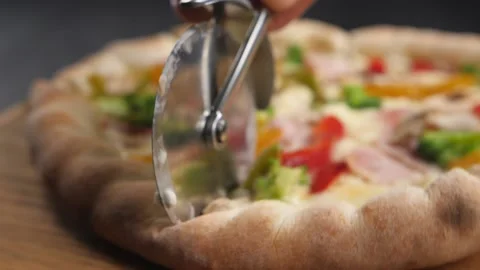 A pizza knife rolls over the surface of a fresh pizza, cutting it. Video stock 195734608