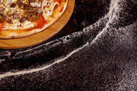 Pizza in the left upper corner on the black background with flour. Copy space. Stock Photos