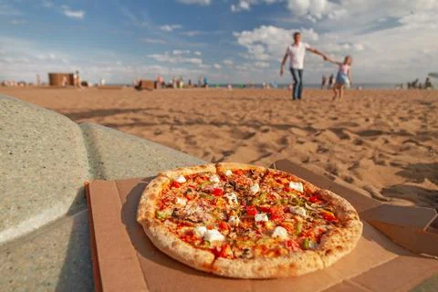 Pizza lies on table in far background happy dad and daughter play in sand in  Stock Photos
