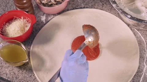The pizza maker adds red sauce to the base of the pizza Stock Footage 158403223