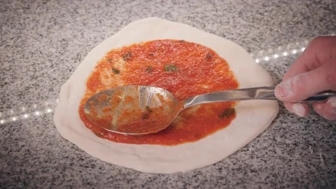 Pizza maker puts ketchup on dough piece smearing with spoon Stock Footage 133359684