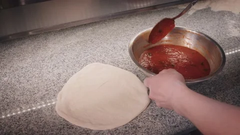 Pizza maker puts tomato sauce on dough using big spoon Stock Footage 133077400
