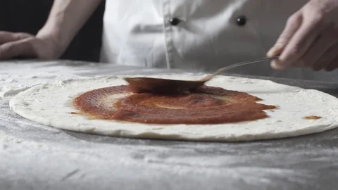Pizza maker spreading tomato sauce on the dough Stock Footage 127414477