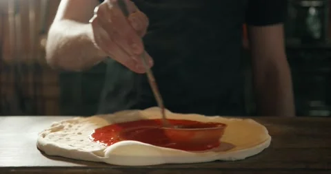 Pizza maker spreading tomato sauce on raw dough for pizza with ladle Vídeo Stock 201467763