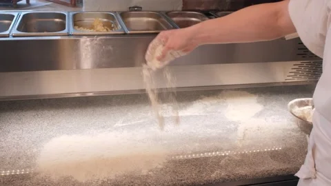 Pizza maker sprinkles flour on kitchen table to roll dough Stock Footage 132473961