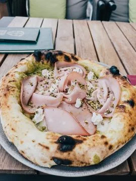 Pizza with mortadella on a thick crust lies on a plate on a wooden table 스톡 사진
