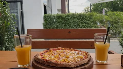 Pizza with pineapple and corn is served on a wooden platter outdoors Stock Footage 313592884