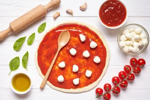 Pizza preparation. Ingredients on the kitchen table: rolled dough with tomatoes Stock Photos