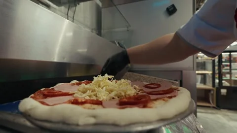 Pizza preparation process featuring a hand in black glove adding cheese and Stock Footage 332736594