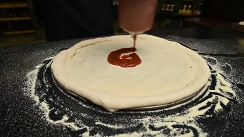 Pizza preparation process: spreading sauce on dough in a kitchen setting Stock Footage 333863796