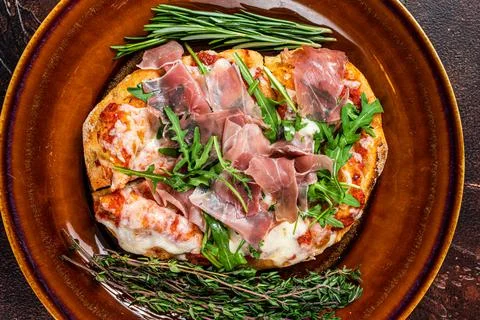 Pizza with prosciutto parma ham, arugula salad and parmesan cheese in a rustic Stock Photos