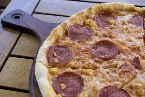 Pizza with salami, pepperoni and corn on wooden table Stock Photos