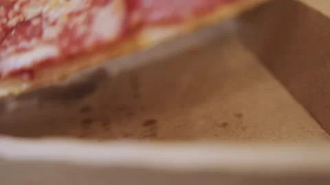Pizza slice lifted. Fingertips touch crust as crumbs fall onto cardboard. Casual Stock Footage 341769426