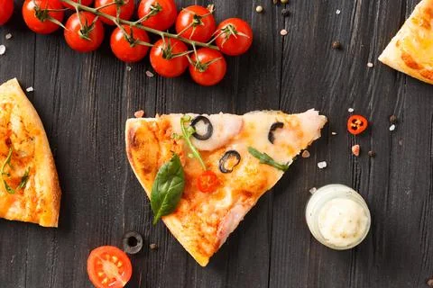 Pizza slices are laid out on a dark background top view. Stock Photos