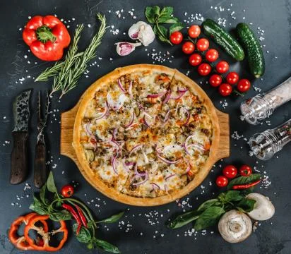 Pizza on the table surrounded by vegetables, herbs and spices Stock Photos