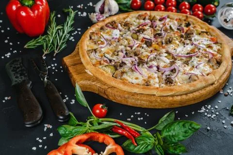 Pizza on the table surrounded by vegetables, herbs and spices Stock Photos