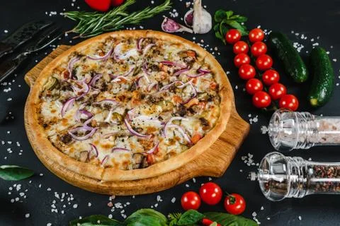 Pizza on the table surrounded by vegetables, herbs and spices Stock Photos