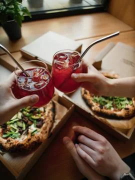 Pizzas in boxes on a table with lemonade in hands, clink glasses Stock Photos