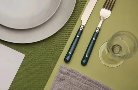 Place setting with plates fork knife and glass on green table Stock Photos