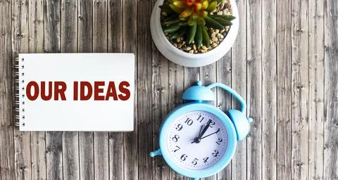 Place of work. Alarm clock, cactus and paper with the text OUR IDEAS on a woo Stock Photos