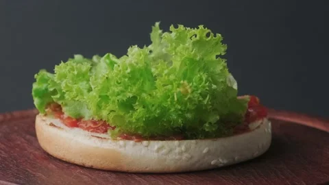 Placing a baked cheeseburger on a bun covered with salad. Stock Footage 140329531