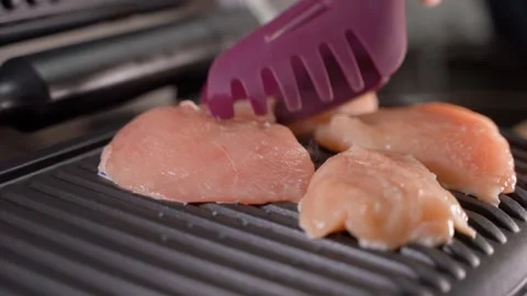 Placing chicken fillet on the hot surface of an electric grill, close-up Stock Footage 323373600