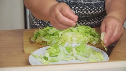 Placing chopped lettuce onto plate for Caesar salad. Arranging fresh greens as Stock Footage 333241528