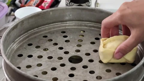 Placing dumplings into a steamer in a kitchen environment with utensils in the 스톡 동영상 343515208