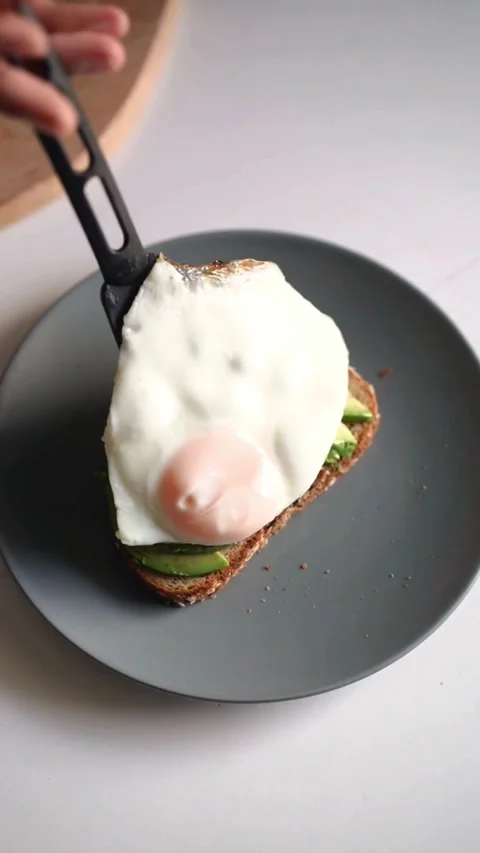 Placing fried egg on avocado toast on gray plate Stock Footage 331771995