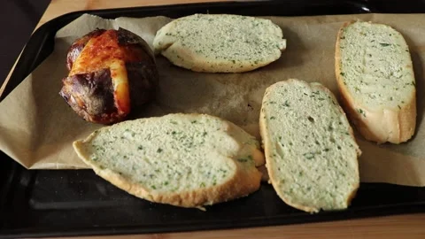 Placing garlic bread onto a oven tray with hot baked potato Video stock 138036225
