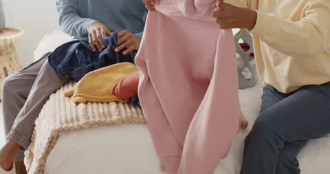 Placing gray laundry basket on bed, African American couple folding hoodie and Stock Footage 346644653