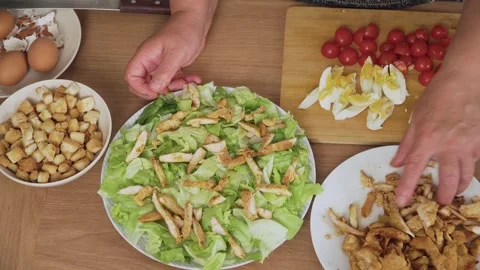 Placing grilled chicken strips onto lettuce base for Caesar salad. Adding cooked Stock Footage 319161720