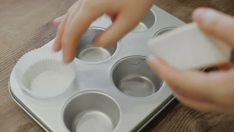 Placing paper cupcake liners into cupcake pan to bake cupcakes Stock Footage 107384076