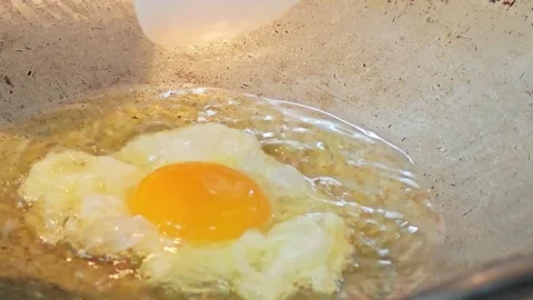 Placing a raw egg yolk onto frying egg white inside a wok. 스톡 동영상 343697946
