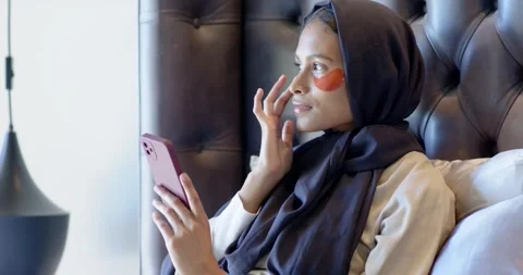 Placing red eye patch for eye care adult hijab-wearing female sitting in bedroom Stock Footage 336059678