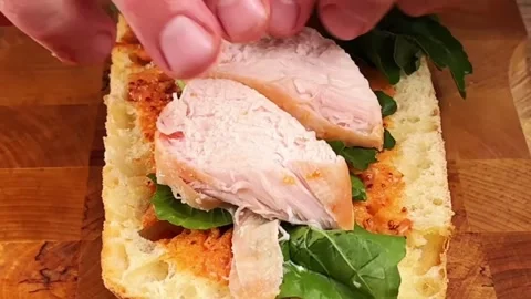 Placing roasted chicken breast slices on ciabatta bread with fresh arugula leave Stock Footage 325032664